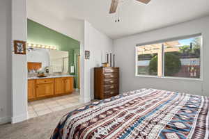 Bedroom with connected bathroom, ceiling fan, light tile patterned flooring, and lofted ceiling