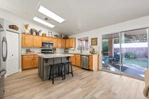 Kitchen with light hardwood / wood-style flooring, a kitchen island, lofted ceiling, and appliances with stainless steel finishes