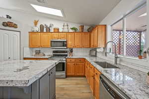 Kitchen featuring appliances with stainless steel finishes, tasteful backsplash, lofted ceiling with skylight, sink, and light hardwood / wood-style floors