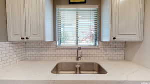 Kitchen featuring white cabinets, decorative backsplash, light stone countertops, and sink