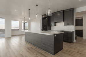 Kitchen with light countertops, hanging light fixtures, an island with sink, and tasteful backsplash