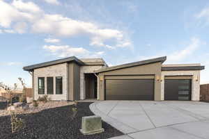 Contemporary house featuring an attached garage, stone siding, concrete driveway, and stucco siding