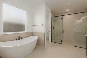 Bathroom with toilet, tile walls, wainscoting, a soaking tub, and a shower stall