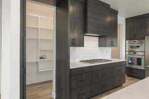 Kitchen with light wood-type flooring, dark brown cabinetry, appliances with stainless steel finishes, and decorative backsplash