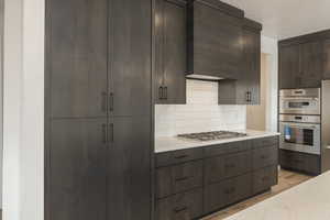 Kitchen with stainless steel appliances, light countertops, backsplash, light wood-style floors, and dark brown cabinets