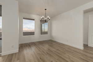 Unfurnished dining area featuring light wood-type flooring, baseboards, and a notable chandelier