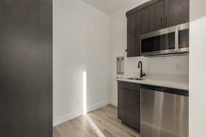 Kitchen featuring stainless steel appliances, dark brown cabinets, light countertops, light wood-type flooring, and a sink