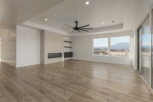 Unfurnished living room featuring light wood-type flooring, a tray ceiling, a glass covered fireplace, and a mountain view