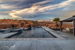 Pool at dusk featuring a patio area, an in ground hot tub, pool water feature, and a mountain view