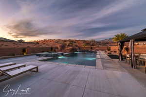 Pool at dusk featuring pool water feature, an in ground hot tub, and a patio