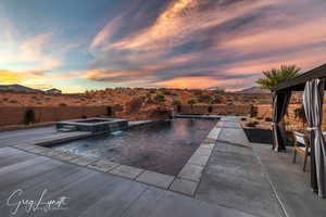 Pool at dusk featuring an in ground hot tub, a mountain view, pool water feature, and a patio