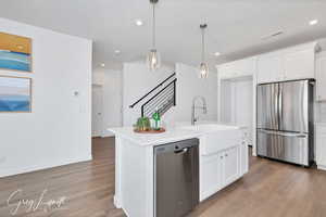 Kitchen featuring appliances with stainless steel finishes, sink, wood-type flooring, white cabinets, and an island with sink