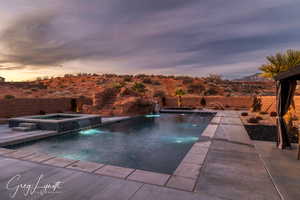 Pool at dusk with pool water feature, a mountain view, and an in ground hot tub