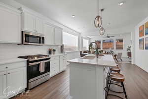 Kitchen featuring white cabinets, stainless steel appliances, a center island with sink, and sink