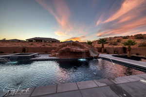 Pool at dusk featuring pool water feature, an in ground hot tub, and a water slide