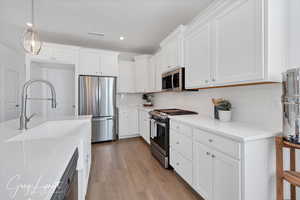 Kitchen featuring white cabinets, appliances with stainless steel finishes, decorative backsplash, and light hardwood / wood-style flooring