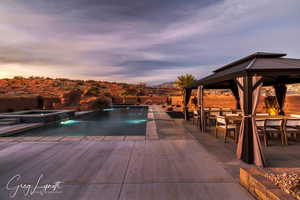 Pool at dusk featuring an outdoor bar, pool water feature, a gazebo, a patio area, and an in ground hot tub