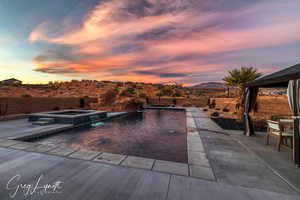 Pool at dusk featuring an in ground hot tub, a mountain view, pool water feature, and a patio