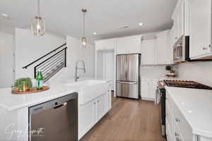 Kitchen featuring decorative light fixtures, wood-type flooring, a kitchen island with sink, and appliances with stainless steel finishes