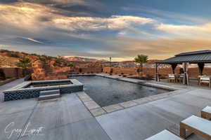 Pool at dusk featuring a gazebo, a mountain view, an in ground hot tub, and a patio