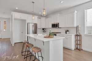 Kitchen featuring white cabinets, decorative light fixtures, appliances with stainless steel finishes, and light hardwood / wood-style flooring