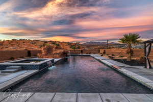 Pool at dusk featuring pool water feature, a mountain view, and an in ground hot tub