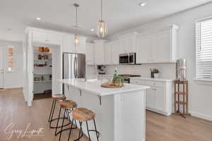 Kitchen featuring white cabinetry, hanging light fixtures, stainless steel appliances, light hardwood / wood-style flooring, and a kitchen island with sink