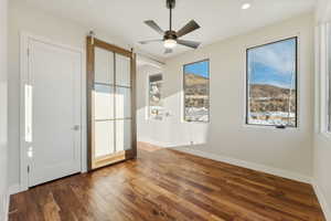 Spare room featuring a barn door, ceiling fan, and dark wood-type flooring