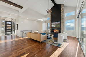 Living room featuring dark wood-type flooring, beam ceiling, high vaulted ceiling, a chandelier, and a stone fireplace