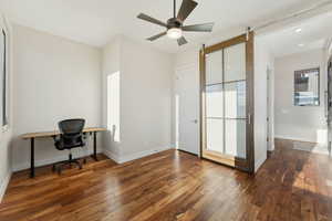 Office area with ceiling fan, a barn door, and dark wood-type flooring