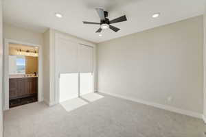 Unfurnished bedroom featuring light carpet, ensuite bathroom, ceiling fan, sink, and a closet