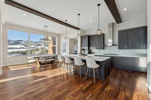 Kitchen with dark wood-type flooring, wall chimney range hood, beamed ceiling, a mountain view, and decorative light fixtures