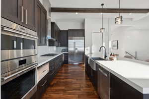 Kitchen featuring hanging light fixtures, sink, appliances with stainless steel finishes, beamed ceiling, and dark hardwood / wood-style flooring