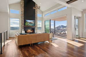 Living room with wood-type flooring, high vaulted ceiling, a stone fireplace, and beam ceiling