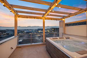 Patio terrace at dusk with a mountain view, a balcony, and a hot tub