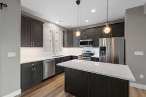 Kitchen with appliances with stainless steel finishes, sink, decorative light fixtures, light hardwood / wood-style flooring, and a kitchen island