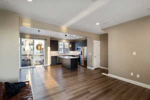 Kitchen featuring appliances with stainless steel finishes, a center island, decorative light fixtures, and dark wood-type flooring