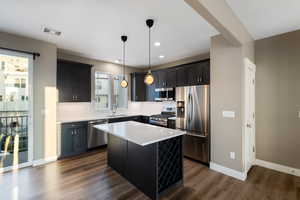 Kitchen featuring appliances with stainless steel finishes, dark hardwood / wood-style flooring, sink, pendant lighting, and a center island