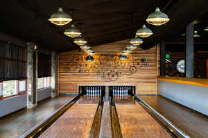 Recreation room with lofted ceiling, wood walls, wood-type flooring, and a bowling alley