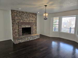 Unfurnished living room featuring a fireplace, a textured ceiling, dark hardwood / wood-style flooring, and a chandelier