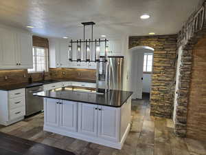 Kitchen with sink, a center island, hanging light fixtures, stainless steel appliances, and white cabinets