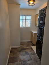 Clothes washing area with a textured ceiling, cabinets, and stacked washer / drying machine