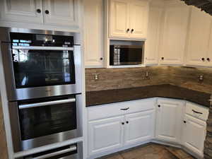 Kitchen featuring backsplash, white cabinets, dark stone counters, and appliances with stainless steel finishes