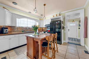 Kitchen with white cabinetry, black refrigerator, a center island, and hanging light fixtures