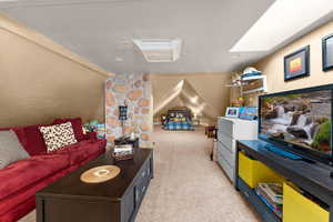 Recreation room with vaulted ceiling with skylight and light carpet