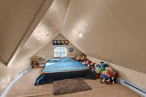 Carpeted bedroom featuring a textured ceiling, vaulted ceiling, and a baseboard heating unit