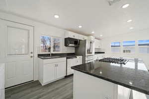 Kitchen with stainless steel appliances, dark wood-type flooring, sink, dark stone countertops, and white cabinets