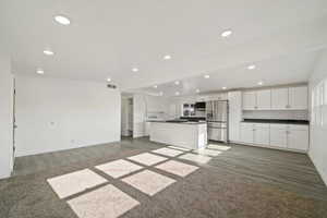 Kitchen with white cabinetry, dark wood-type flooring, tasteful backsplash, stainless steel refrigerator with ice dispenser, and a center island with sink