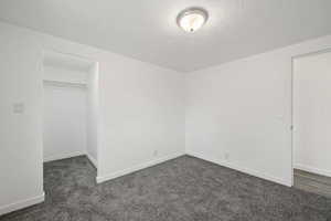 Unfurnished bedroom with a textured ceiling, dark carpet, and a closet