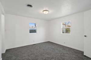 Spare room featuring dark colored carpet, plenty of natural light, and a textured ceiling